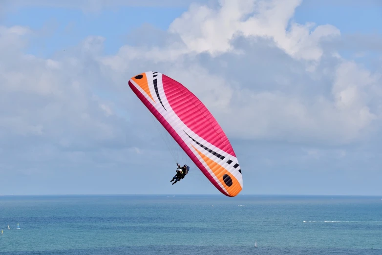 a person parasailing over the ocean on a sunny day, a picture, by Julian Allen, shutterstock, ornithopter, black and yellow and red scheme, 3 meters, on the coast