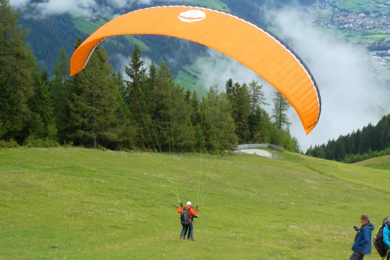 a couple of people standing on top of a lush green field, a picture, by Werner Andermatt, shutterstock, parachutes, orange grey white, view from the side, canopy