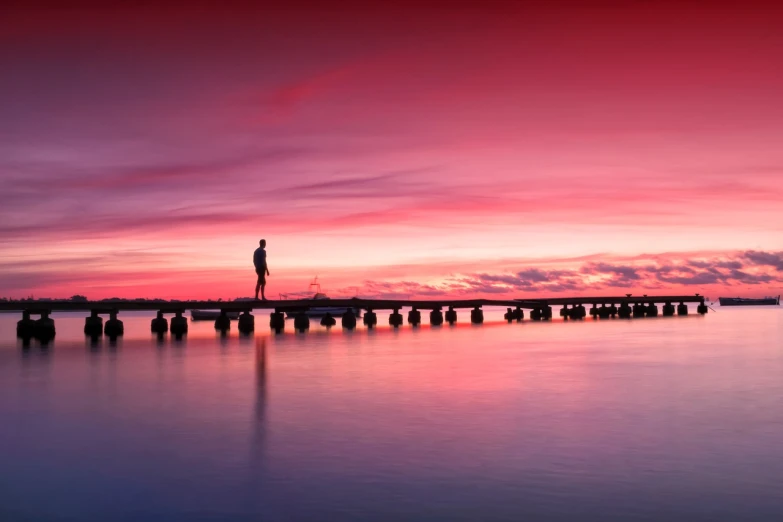 a lighthouse sitting on top of a pier next to a body of water, by Holger Roed, pexels contest winner, romanticism, redpink sunset, man standing, panoramic photography, vine bridge silhouette over lake