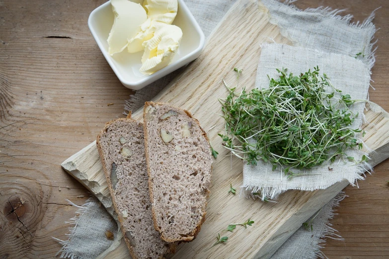 a piece of bread sitting on top of a wooden cutting board, inspired by Kalervo Palsa, sprouting, butter, herbs, adi meyers