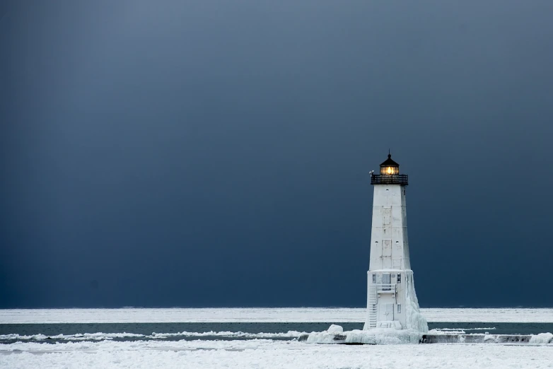 a white lighthouse sitting on top of a snow covered beach, by Andrew Domachowski, in a lighting storm, ice, narrow, former