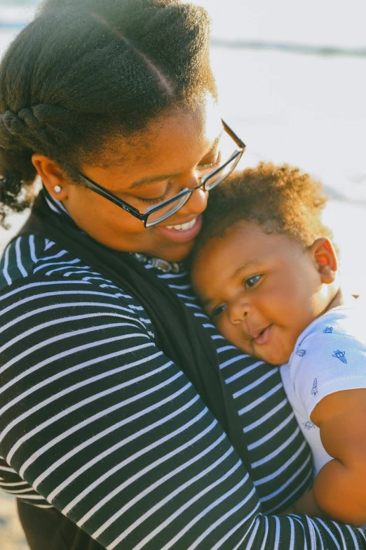 a woman holding a child on the beach, by Lily Delissa Joseph, pexels, avatar image, african american, big cheeks, closeup - view