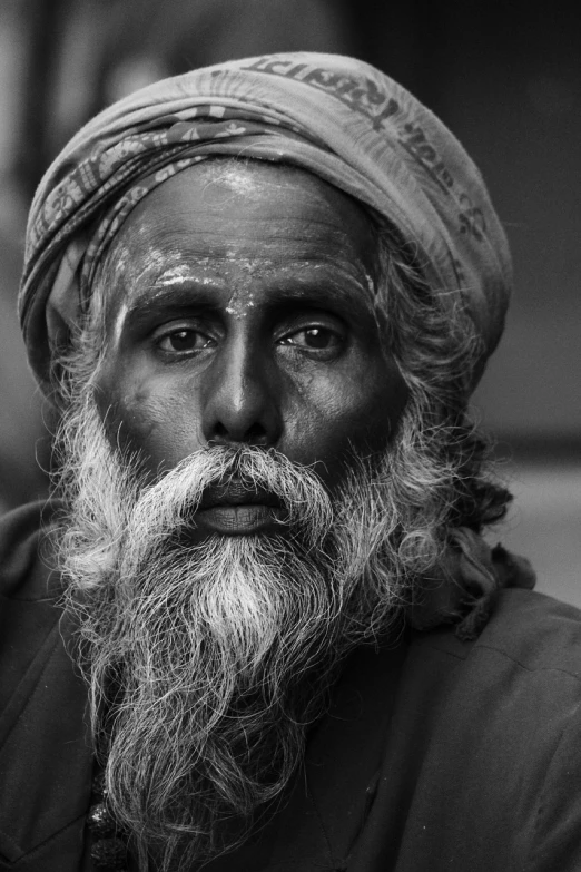 a man with a long beard wearing a turban, a black and white photo, by Sudip Roy, pexels contest winner, close - up shots of faces, druid portrait, innocent look. rich vivid colors, man with thin lines on the face