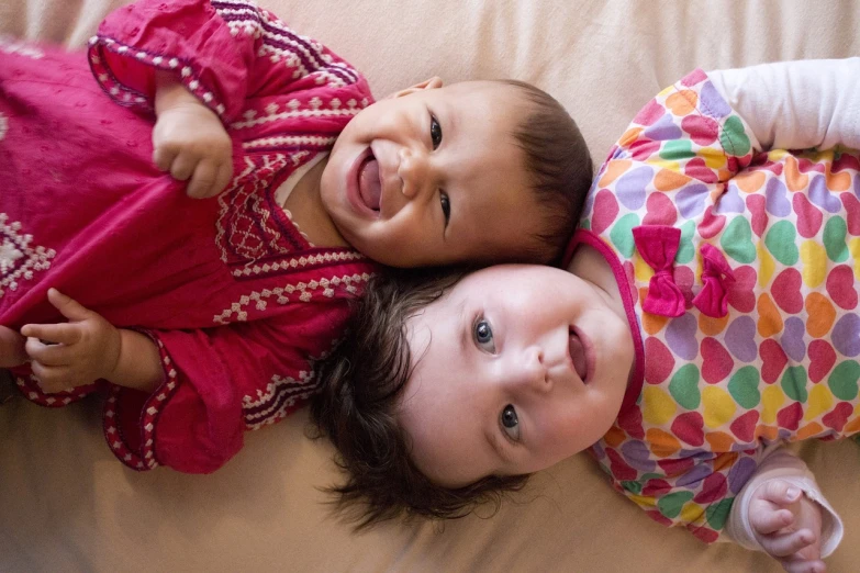 a couple of babies laying on top of a bed, by Juan O'Gorman, flickr, incoherents, big smile on her face, islamic, beautiful highly symmetric faces, a colorful