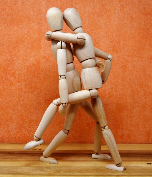 a couple of wooden mannequins standing next to each other, trending on pixabay, figuration libre, playful pose of a dancer, injured, hugging each other, indoor picture