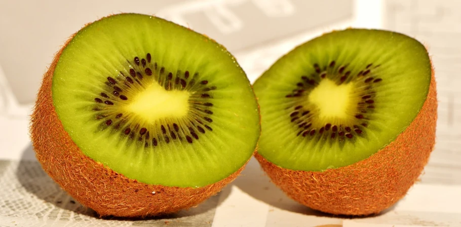 two pieces of kiwi sitting on top of a newspaper, inspired by Kōno Michisei, pixabay, hurufiyya, fresh fruit, symmetry!, uwu hi-fructose, zoomed in