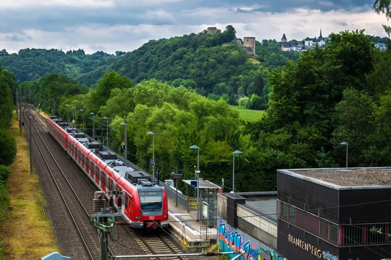 a red train traveling down train tracks next to a forest, german romanticism, outdoors european cityscape, hills, terminal, detmold