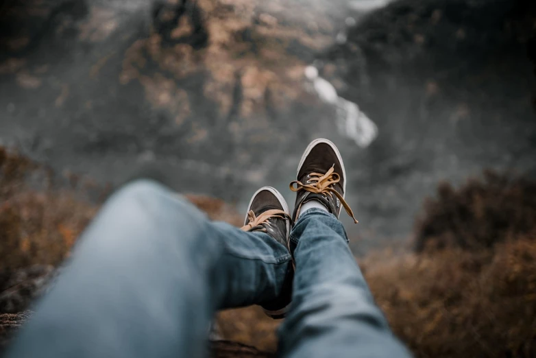 a person sitting on a rock with their feet up, pexels contest winner, realism, blue jeans and grey sneakers, towering high up over your view, 🤬 🤮 💕 🎀, relaxing after a hard day