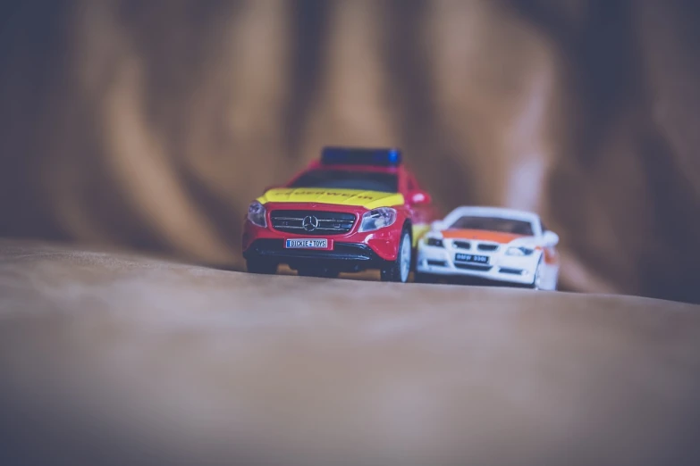 two toy cars sitting next to each other on a bed, a tilt shift photo, ambulance, mercedes, miniature product photo, flash photo