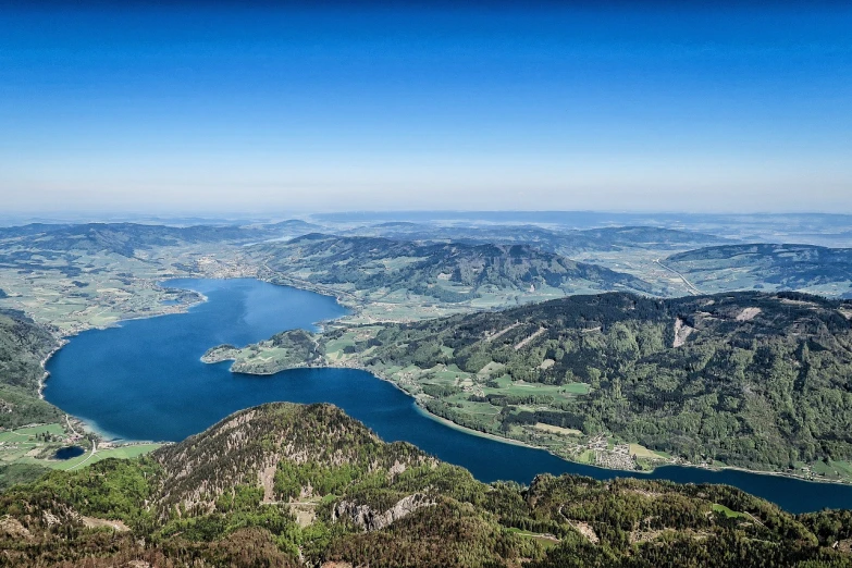 a large body of water sitting on top of a lush green hillside, by Jakob Gauermann, shutterstock, bird\'s eye view, mountains and lakes, ultra wide horizon, surrounding the city