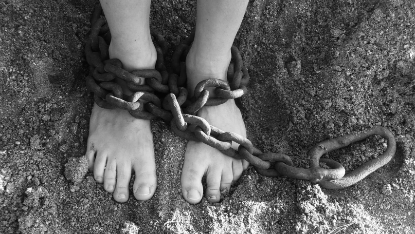 a pair of feet chained to a chain, a black and white photo, pixabay, arrested, wrapped in black tentacles, childhood, wikimedia commons