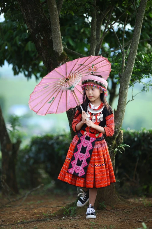 a little girl standing under a tree holding a pink umbrella, inspired by Miao Fu, dau-al-set, tribal clothing, authentic costume, red adornments, a potrait of a beautiful