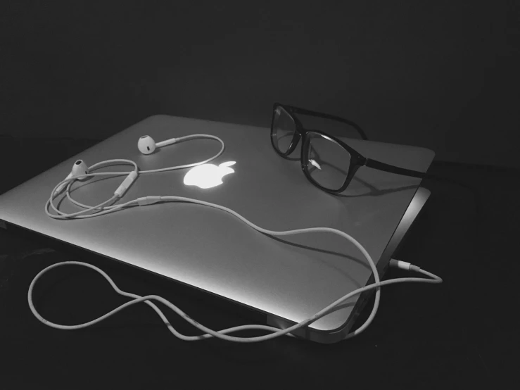 a laptop computer sitting on top of a table, a black and white photo, by Mirko Rački, black rimmed glasses, uneven glass apple in the dark, black wired cables, listening to music at 2 am