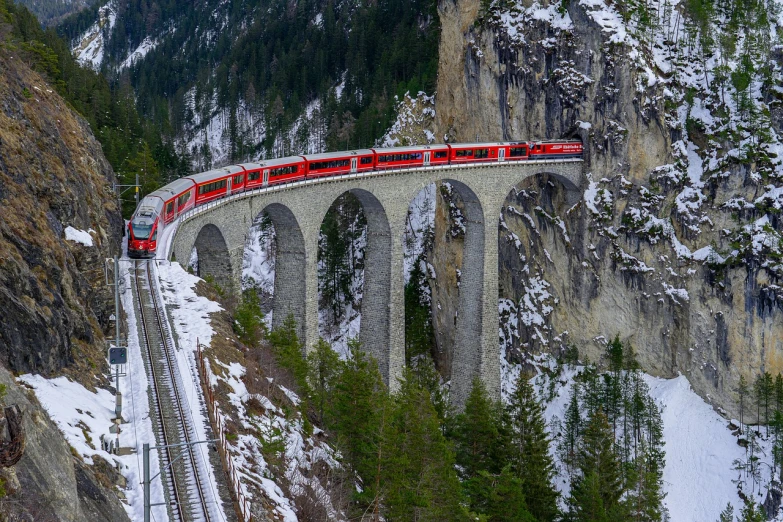 a red train traveling over a bridge in the mountains, by Karl Stauffer-Bern, shutterstock contest winner, aqueduct and arches, cold but beautiful, shot from 5 0 feet distance, istockphoto