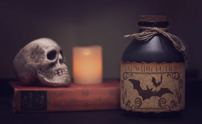 a bottle sitting on top of a table next to a candle, gothic art, ancient evil letters, toned paper, trick or treat, cover shot