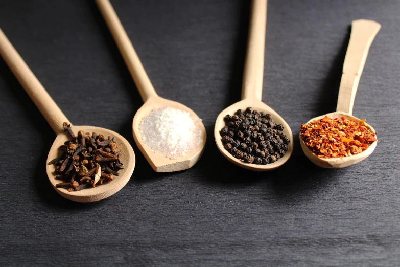 five wooden spoons filled with different kinds of spices, a screenshot, pexels, dau-al-set, against a deep black background, pork, poppy, sansa