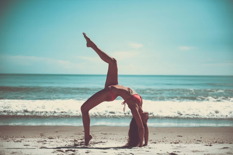 a woman doing a handstand on the beach, a picture, tumblr, arabesque, cropped red yoga short, vintage color, pretty face with arms and legs, brunette fairy woman stretching