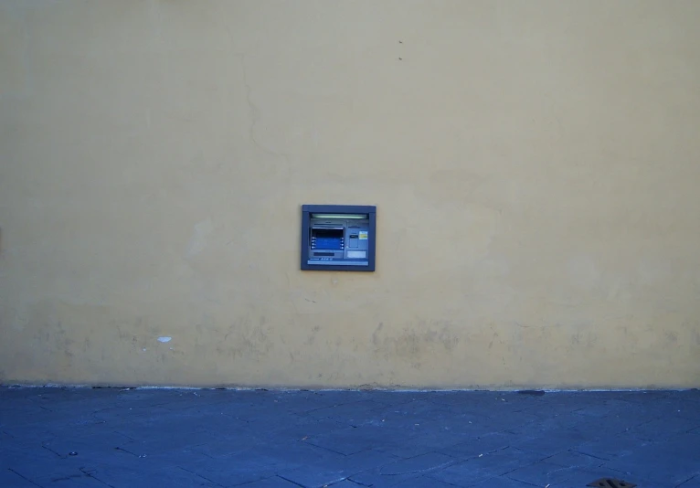 an atm machine on the side of a building, inspired by Telemaco Signorini, flickr, postminimalism, florence, lcd screen, before a stucco wall, blue and yellow