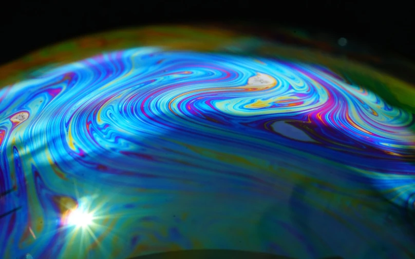 a close up of a colorful object on a table, flickr, holography, swirling liquids, full sun, reaction-diffusion pattern, leaking oil
