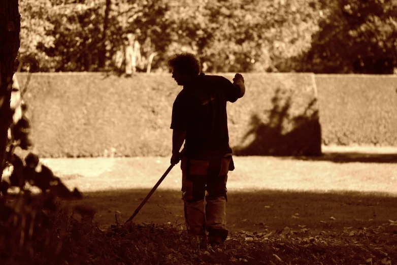 a man holding a baseball bat standing next to a tree, inspired by August Sander, flickr, tonalism, mowing of the hay, autum garden, silhouette!!!, bronze