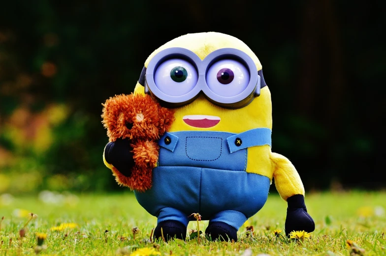 a yellow and blue minion holding a teddy bear, a picture, pixabay, lawn, 🦩🪐🐞👩🏻🦳, plushie photography, stock photo