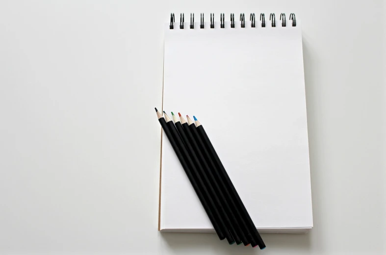 a notebook with three colored pencils next to it, a drawing, minimalism, white and black, product introduction photo, black-and-white, crisp photo