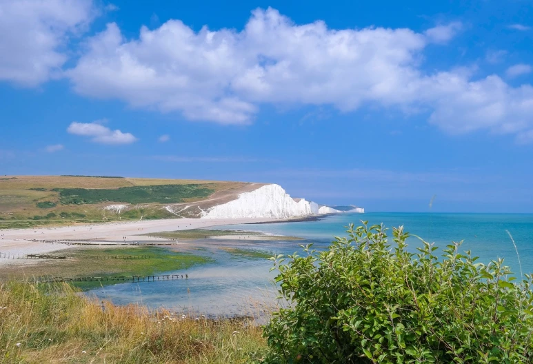 a large body of water sitting next to a lush green hillside, a stock photo, shutterstock, cliffs of dover, on a bright day, seaside backgroud, best selling