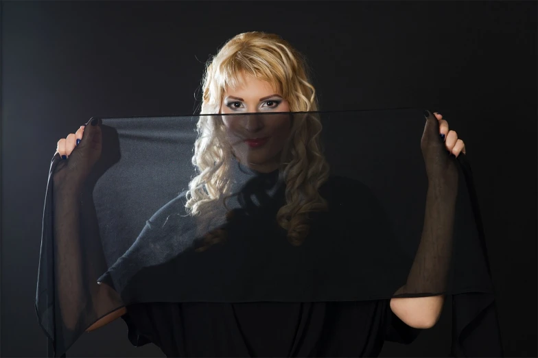 a woman holding up a picture of herself, inspired by Anna Füssli, realism, vantablack cloth technology, young blonde woman, transparent veil, on a dark background