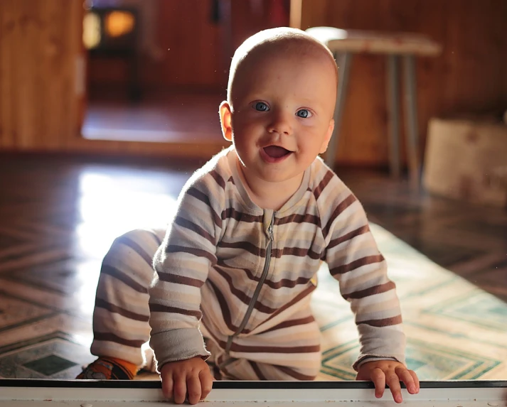 a baby sitting on the floor looking at the camera, a picture, by Tom Carapic, pixabay, sunlit, on a wooden table, happy grin, stripes