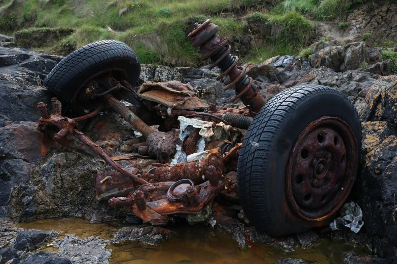 a rusted car sitting on top of a pile of rocks, by Thomas Furlong, flickr, covered with liquid tar. dslr, wheel, with damaged rusty arms, marsden