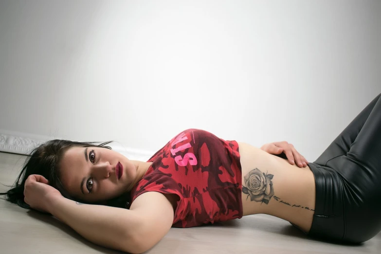 a woman laying on the floor with a tattoo on her stomach, a tattoo, by Ludovit Fulla, outfit photo, shot on webcam, red hot, on a white table