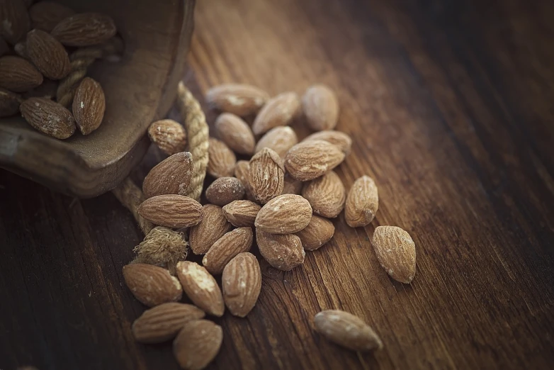 a wooden spoon filled with almonds on top of a wooden table, a picture, renaissance, [ realistic photography ], smooth in _ the background, digitally enhanced, snacks