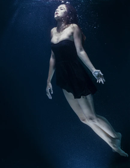 a woman in a black dress swims under water, a portrait, inspired by Brooke Shaden, unsplash, dark blues, production still, medium format. soft light, leg shot
