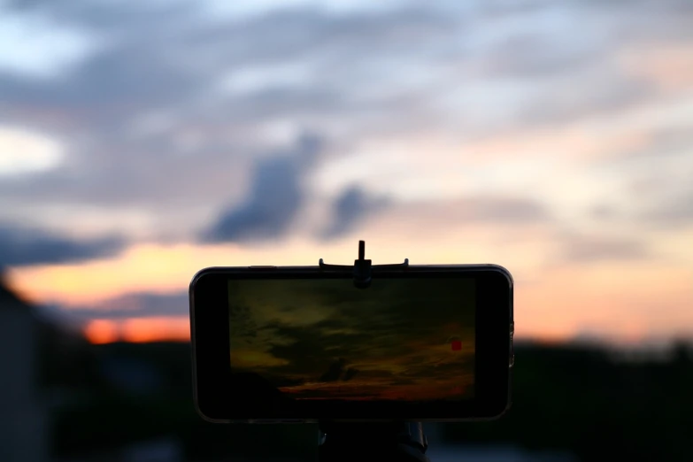 a cell phone sitting on top of a tripod, a picture, by Tom Carapic, happening, cloudy sunset, 4 k product photo, movie footage, long exposure photo