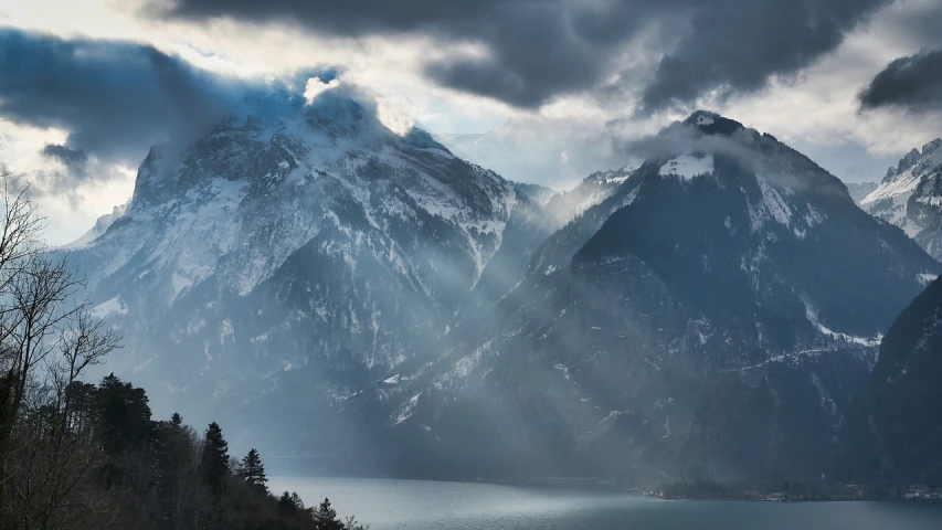 a large mountain covered in snow next to a body of water, a picture, by Sebastian Spreng, pexels contest winner, romanticism, sunlight breaking through clouds, today\'s featured photograph 4k, dark misty foggy valley, light blue mist