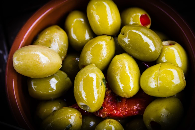 a bowl filled with green olives sitting on top of a table, a picture, inspired by Ceferí Olivé, shutterstock, olive green and venetian red, close-up product photo, panini, glazed