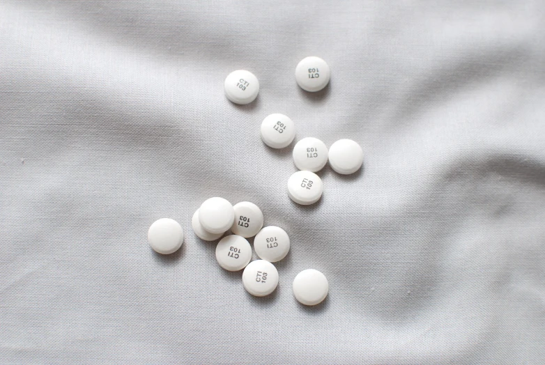 a bunch of pills sitting on top of a white sheet, a photo, by Emma Andijewska, antipodeans, white color scheme, bts, studio shot, buttons