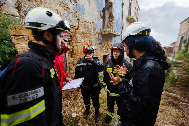 a group of people standing in front of a building, by Luis Molinari, shutterstock, young female firefighter, examining ruins, greek, high quality image”