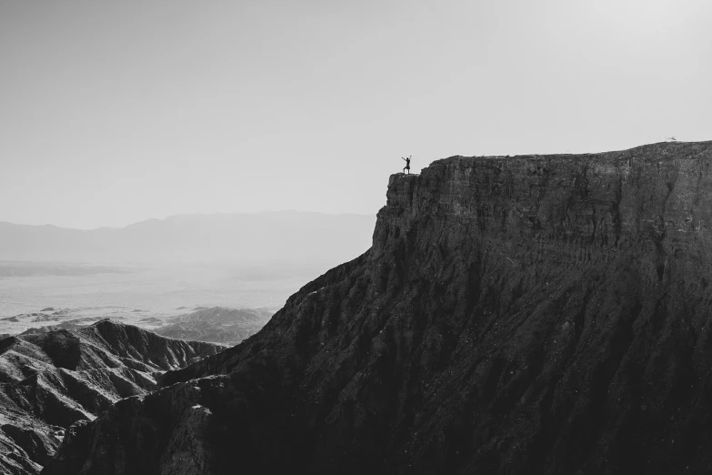 a black and white photo of a person standing on top of a mountain, unsplash contest winner, fine art, tucson arizona, sharp cliffs, an arab standing watching over, running at the edge of space