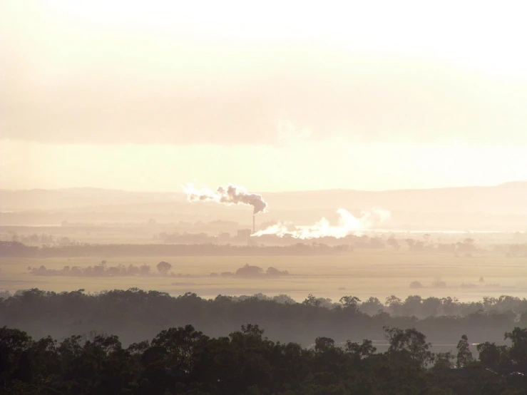 a view of a field with smoke coming out of it, by Lee Loughridge, flickr, figuration libre, tamborine, factories and nature, viewed from bellow, early morning light