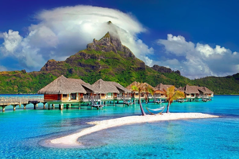 a group of huts sitting on top of a beach next to a body of water, a picture, shutterstock, polynesian style, background image, wallpapers, azure blue water