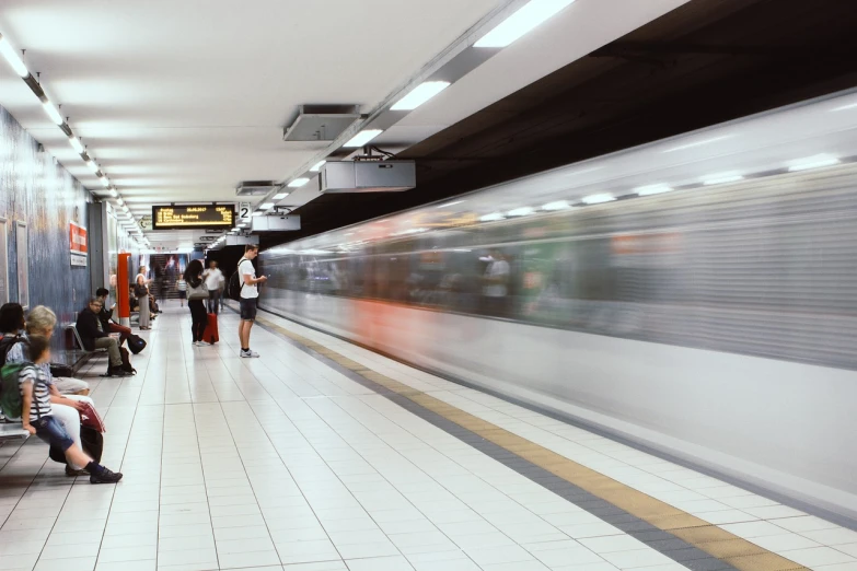 a group of people sitting on a bench next to a train, a picture, by Emma Andijewska, shutterstock, motion blur of people walking, in sao paulo, underground facility, low ultrawide shot