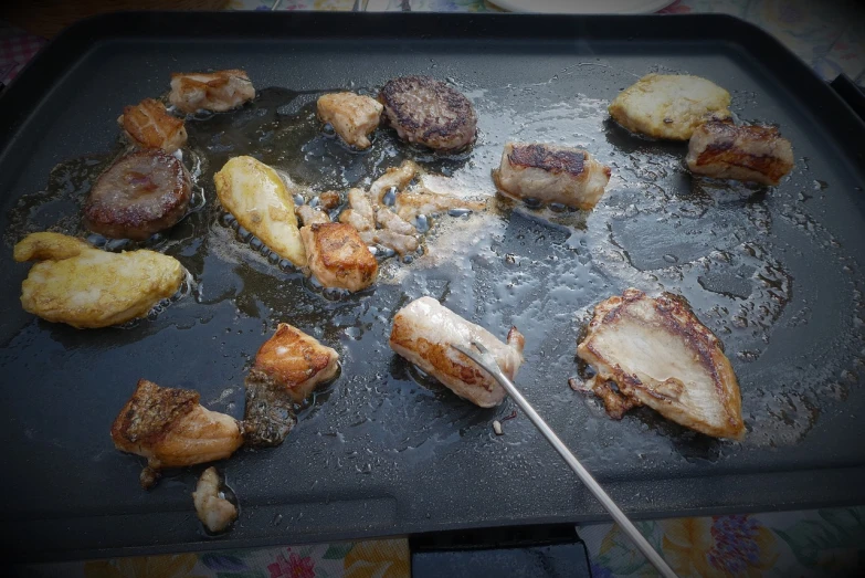 a pan filled with meat and potatoes on top of a table, by Géza Udvary, baroque, barbecuing chewing gum, low quality photo, outdoor photo, abalone