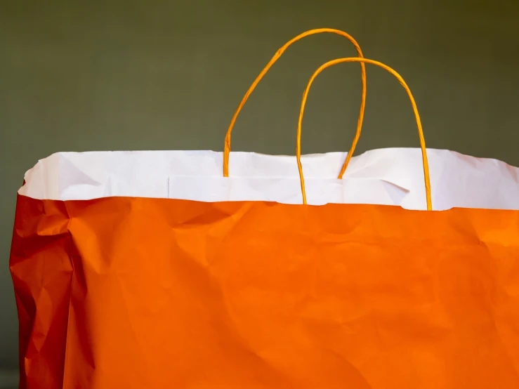 a paper bag sitting on top of a table, a photo, minimalism, orange details, close-up product photo, detailed zoom photo, huge details