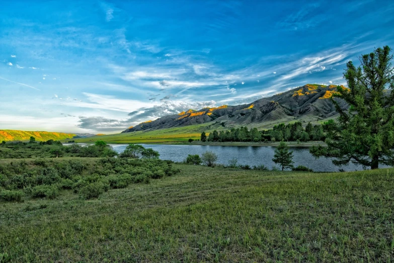 a body of water sitting on top of a lush green field, by Koloman Sokol, shutterstock, mongolia, 8k hdr dusk light, mountains river trees, hdr photo