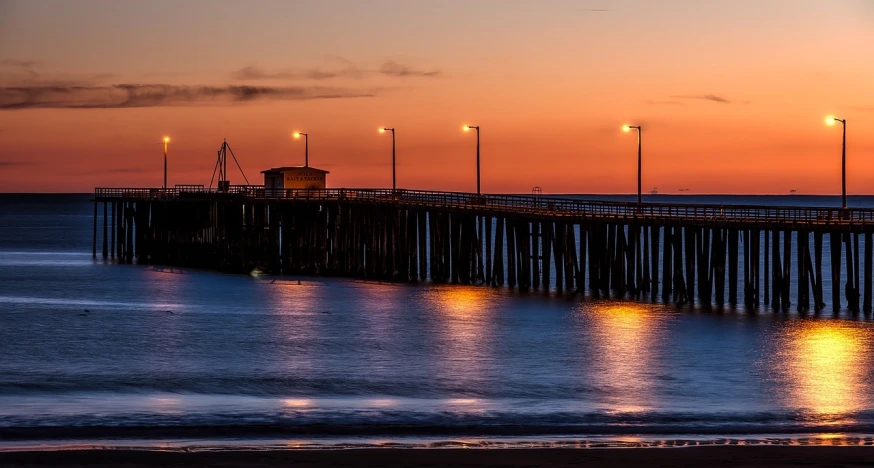 a pier sitting on top of a beach next to the ocean, a portrait, by Dave Melvin, with orange street lights, golden hour in pismo california, 6 4 0, uncropped