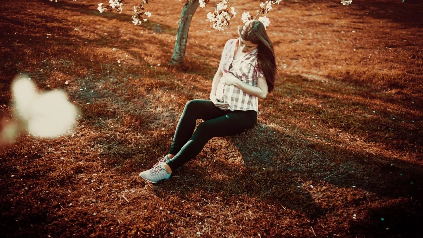 a woman sitting on top of a lush green field, a picture, inspired by Elsa Bleda, tumblr, art photography, under sakura tree, sneaker photo, sepia sunshine, pregnancy