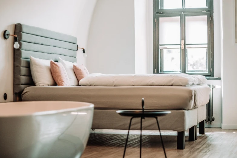 a bed sitting in a bedroom next to a bathtub, by Matija Jama, pexels, taupe, furniture design, thumbnail, glossy surface