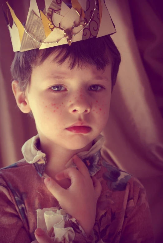 a young boy with a paper crown on his head, a portrait, inspired by Diane Arbus, pexels, digital art, rosy cheeks with freckles, a medieval, retro effect, the little prince