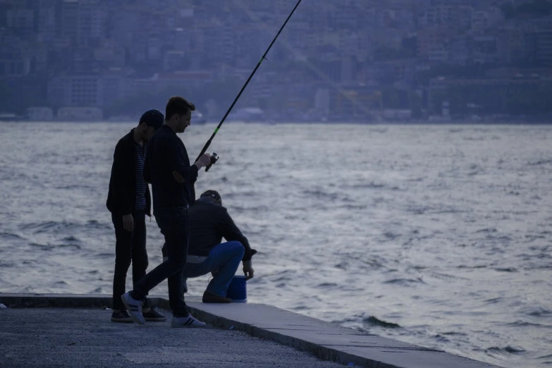 a couple of men standing on top of a pier next to a body of water, a picture, shutterstock, people angling at the edge, istanbul, harsh flash photo, stock photo